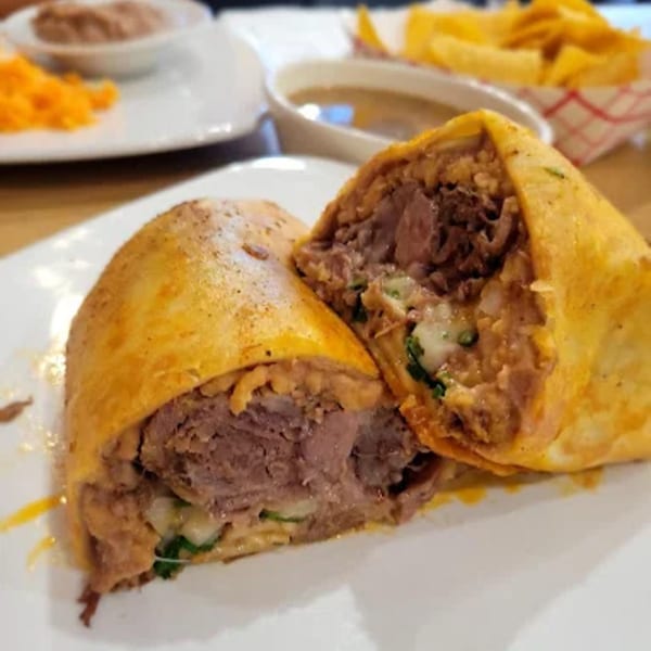 A Hacienda Jalisco burrito, cut in half, revealing beef, cheese, and other fillings, with sides in the background.