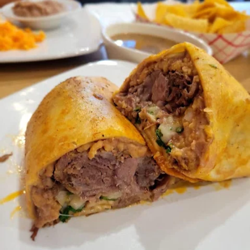 A Hacienda Jalisco burrito, cut in half, revealing beef, cheese, and other fillings, with sides in the background.