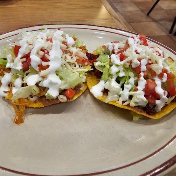 Two Hacienda Jalisco tostadas topped with shredded chicken, lettuce, tomatoes, cheese, and sour cream.
