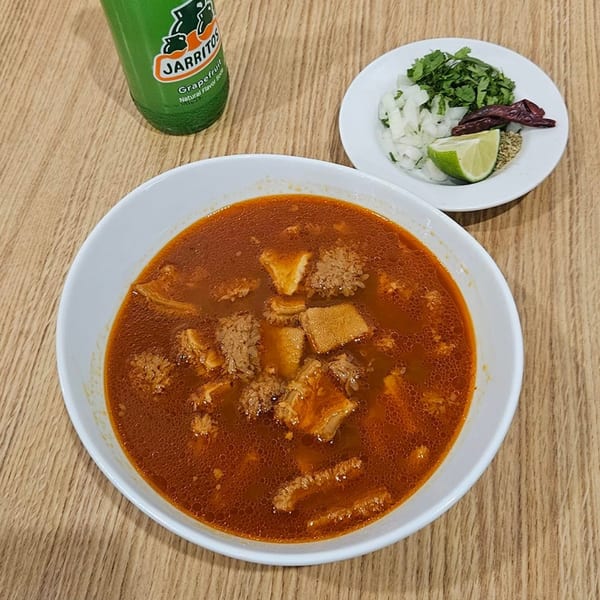 Menudo soup with a side of chopped onions, cilantro, lime, and dried chiles, with a Jarritos soda.