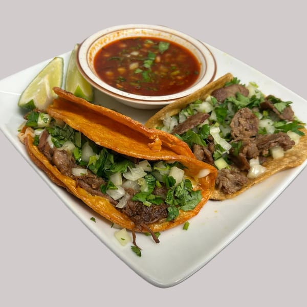 Two Hacienda Jalisco birria tacos with cilantro and onions, served with a side of consommé and lime.