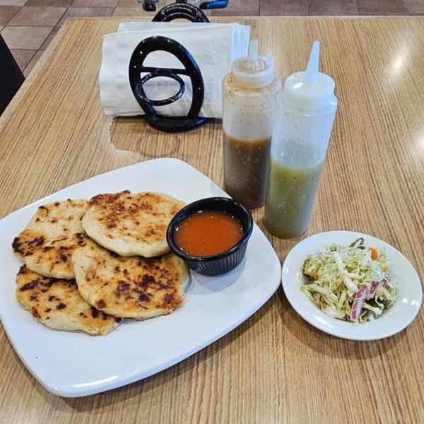 Hacienda Jalisco's pupusas with red sauce, green and brown salsas, and a side salad on a wooden table.